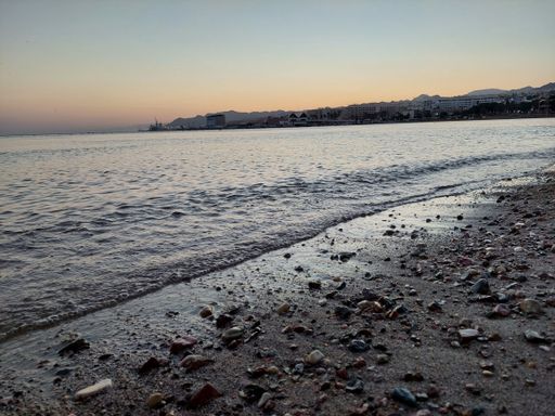 A rocky shoreline illuminated by the setting sun, with gentle waves lapping against the shore.