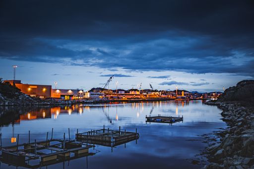 A river surrounded by buildings and lights under a cloudy sky in the evening