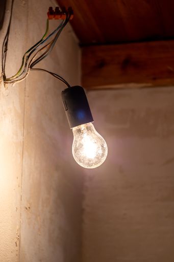 A vertical shot of a light bulb hanging from wires on a wall with a blurry background