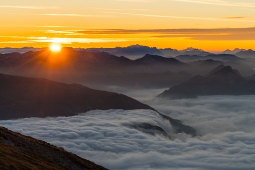 A landscape of rocky hill silhouettes covered in the fog under the sunlight during a beautiful sunset