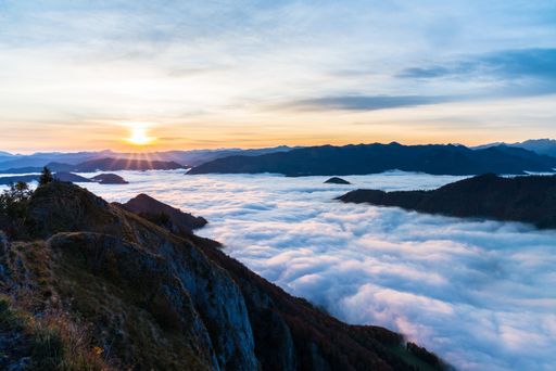 A landscape of rocky hill silhouettes covered in the fog under the sunlight during a beautiful sunset