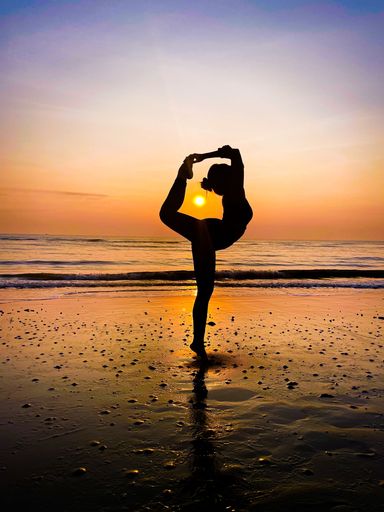 A vertical shot of a female silhouette doing the Natarajasana yoga pose at the beach with the sunset in the background