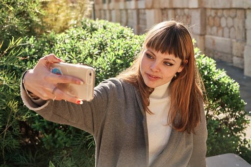 A selective focus shot of a beautiful cheerful young lady with bangs taking a selfie outdoors