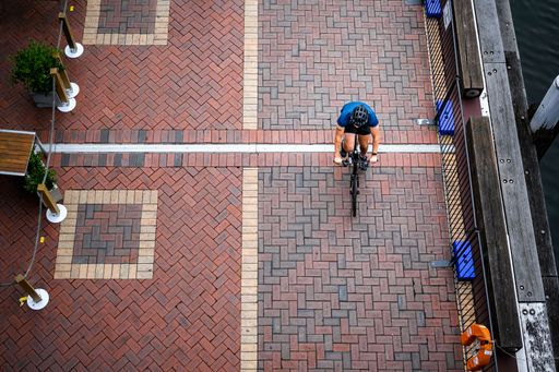 An overhead shot of a man cycling along the pavement in Darling Harbour in the late afternoon