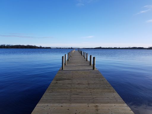 A wooden pier stretching out into the water with a blue sky in the background
