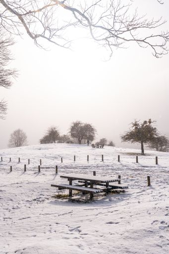 A vertical shot of a picnic area with benches covered by snow on the peak of Mount Aizkorri, Gipuzkoa