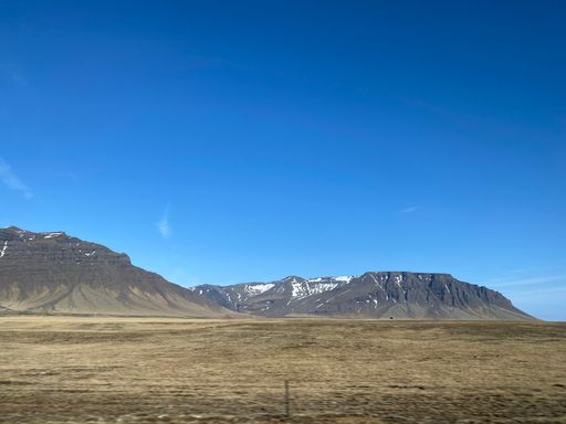 A scenic view of a wide mountain road, surrounded by lush green hills, stretching out into the horizon