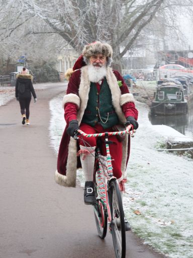 A vertical shot of a Santa cycling along the river