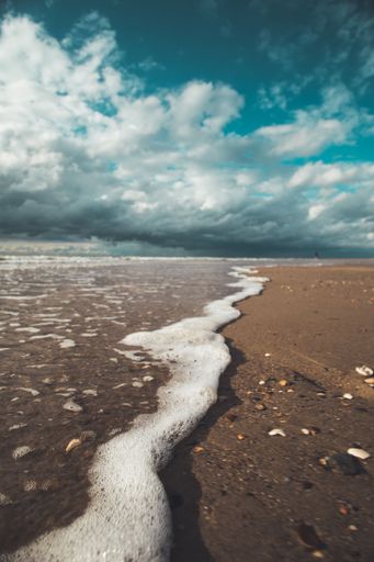 A closeup shot of bubbling waves washing the coast under the blue sky and clouds