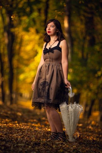 A vertical shot of a beautiful woman in a vintage dress holding an umbrella standing in a park