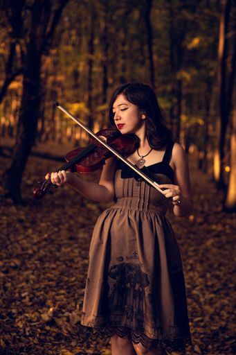 A vertical shot of a beautiful woman in a vintage dress playing the violin in the park