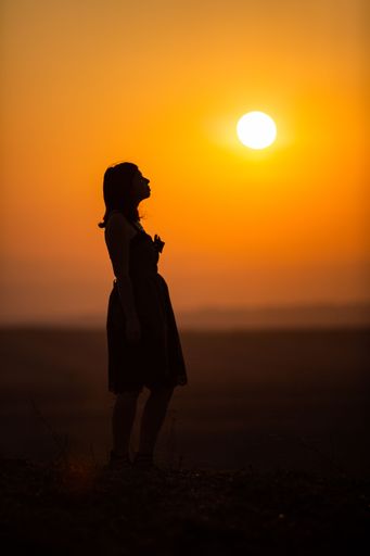 A vertical shot of a silhouette of a woman in a dress with an orange sunset in the background