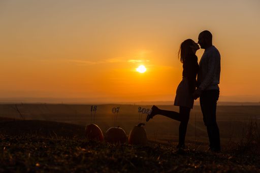 A cute couple holding hands and kissing at sunset with their marriage date in the background