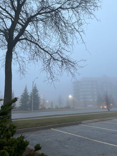 A vertical shot of an outdoor parking lot with buildings in the background on a foggy weather