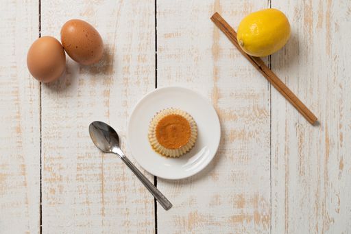 A top view closeup of a plate of Creme Caramel dessert, cinnamon, lemon, and eggs on the white plank table