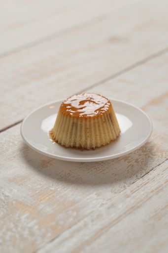 A vertical closeup of a plate of Creme Caramel dessert on a white plank table