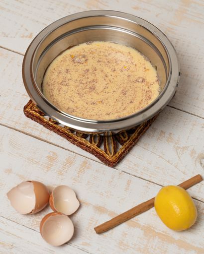 A vertical shot of a bowl of mixed ingredients, cracked eggshells, lemon, and cinnamon on a plank table