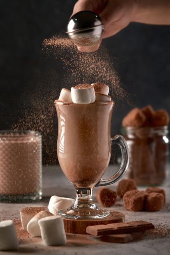 The hand sprinkles cocoa powder on the marshmallow latte.