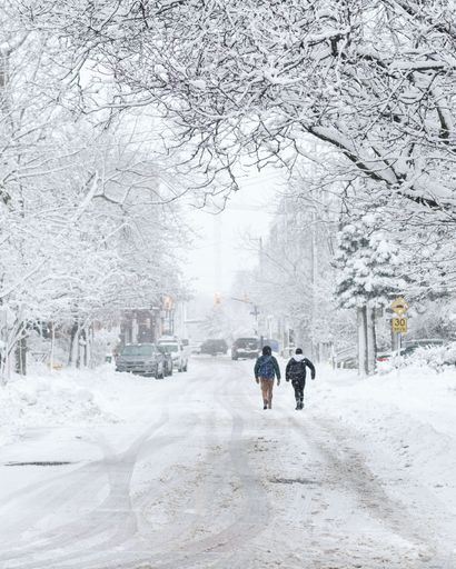 A back view of two young kids with backpacks walking along a snowy street with white trees in Ottawa