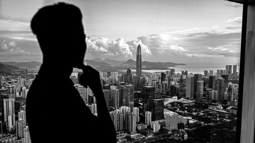 A grayscale shot of a silhouette of a person looking through the window with the view of Shenzen city.