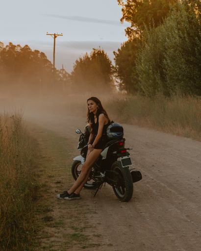 A vertical shot of a cool girl sitting on a motorcycle with a helmet in the countryside