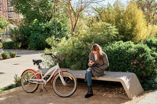 A young pretty caucasian female sitting outdoors next to her bike and using her phone