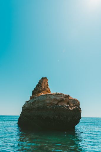 A vertical shot of a rocky cliff in the sea under the bright sky