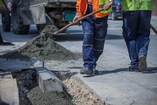 A workers with uniforms filling the hole with cement for installing a sidewalk later