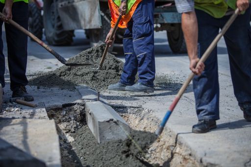 A workers with uniforms filling the hole with cement for installing a sidewalk