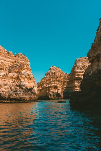 A vertical shot of rocky cliffs reflecting on the sea on a sunny day
