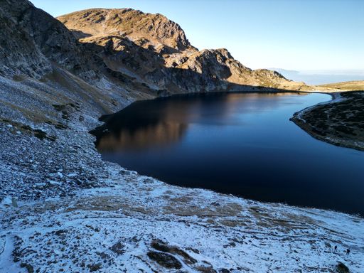 An aerial view of a frozen lake surrounded by large rocks, with snow-capped mountains in the background