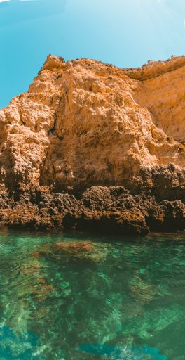 A vertical shot of a rocky cliff reflecting on the sea on a sunny day