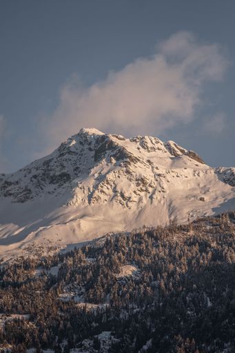 A vertical shot of the Alps covered in snow on a sunny day with a cloudy blue sky in the background