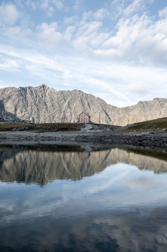 A vertical shot of a house in front of a lake reflecting the cloudy blue sky