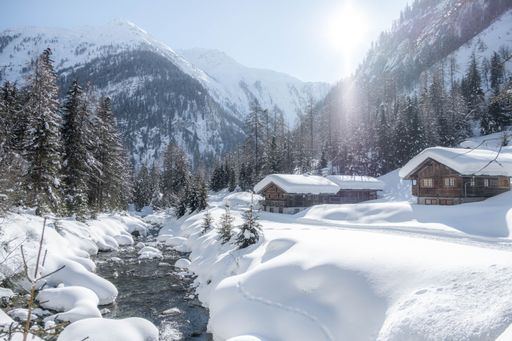 The wooden houses covered in snow with mountains in the background on a sunny day