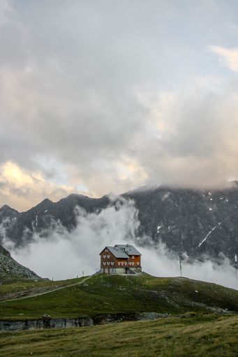 A vertical shot of a beautiful house with mountains and a cloudy sky in the background