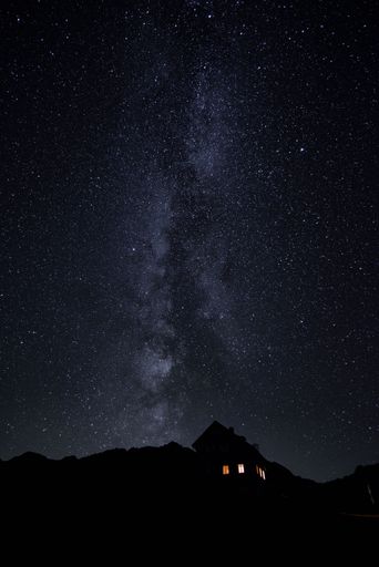 A vertical shot of a house at night with a sky full of bright stars in the background