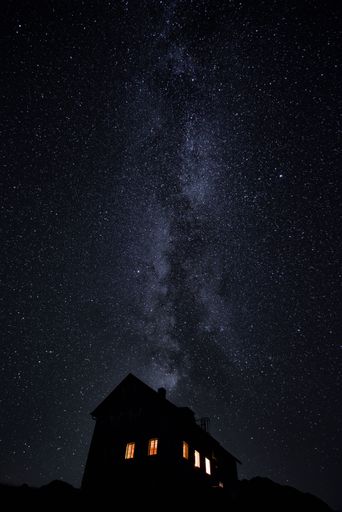 A vertical shot of a house at night with a sky full of bright stars in the background
