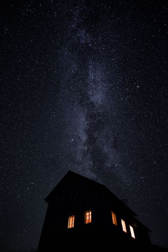 A vertical shot of a house at night with a sky full of bright stars in the background