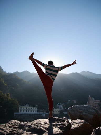 A vertical shot of a young man standing on a rock with one leg