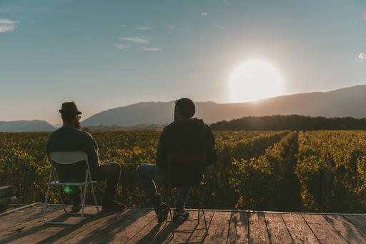 A silhouette of two men sitting and talking looking at the field before sunset