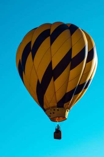 A beautiful yellow and blue hot air balloon flying high against a blue sky
