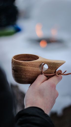 A man holding a crafted wooden cup against blurry snow field