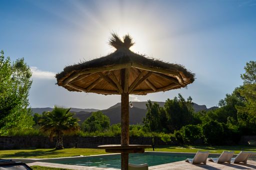 A closeup shot of an umbrella and a pool on a sunny day near a mountain