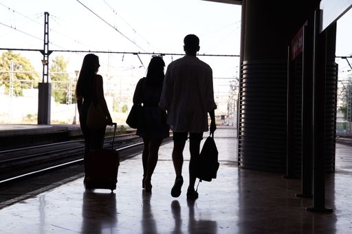 a Silhouette of a group of people walking through the train station. three unrecognizable young men with travel bags