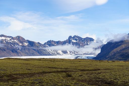 An expansive grassy field stretches across the landscape, with distant mountains in the background