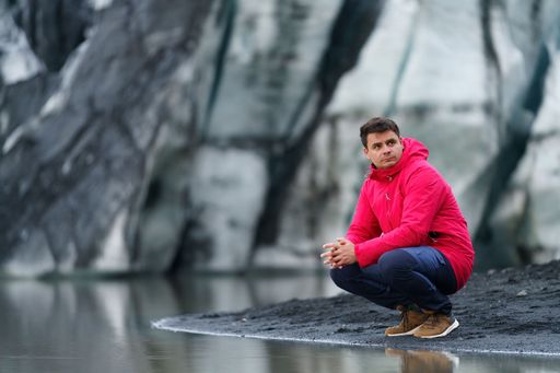 A beautiful shot of a Caucasian male next to a lake with mountain ragged rock formations in background