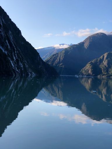 A vertical shot of a calm lake with the big mountains reflected in the waters on a sunny day