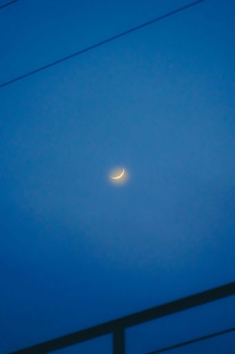 A vertical shot of the blue night sky with the waning crescent moon shining in the middle