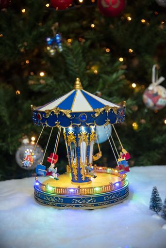 A vertical shot of a child carousel ornament with the decorated Christmas tree in the background